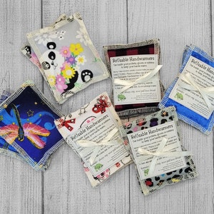 May include: Six reusable hand warmers with different fabric patterns. The hand warmers are made of fabric and have a white label with the text "Reusable Handwarmers" and instructions for use. The hand warmers are tied with a white ribbon.