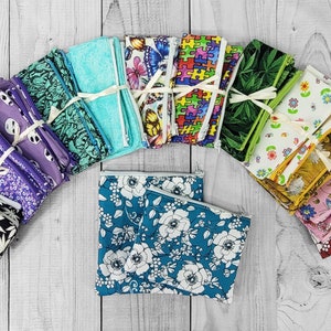 Peut inclure: Une collection de 18 sacs à sandwich réutilisables en tissu. Les sacs sont de différentes couleurs et motifs, notamment des motifs floraux, géométriques et abstraits. Les sacs sont disposés en demi-cercle sur une surface en bois.