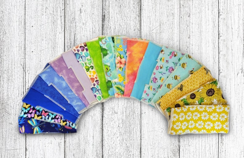 May include: A collection of 16 colorful fabric squares with various patterns, including butterflies, flowers, bees, and geometric designs. The squares are arranged in a semi-circle shape, with the yellow squares at the bottom.
