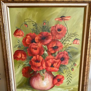 May include: Oil painting of a bouquet of red poppies in a pink vase, set against a green backdrop. The artwork is framed in a gold-colored, ornate frame. The painting has a vintage aesthetic.