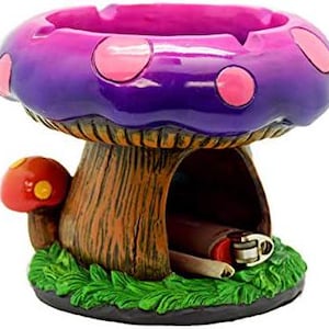 May include: Purple and pink mushroom shaped ashtray with a brown mushroom base and a slot for a lighter. The ashtray has a green grass base.