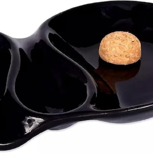 May include: Black ceramic ashtray with two separate compartments and a raised center section. The ashtray is shaped like a fish.