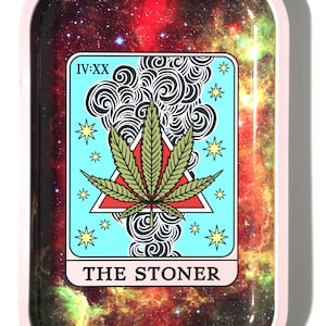 May include: A pink metal rolling tray with a galaxy print featuring a tarot card design. The card is blue with a green marijuana leaf in a red triangle and the text "THE STONER" at the bottom.