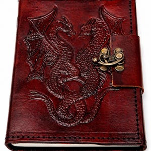 May include: A burgundy leather journal with a detailed embossed design of two dragons facing each other. The journal has a clasp closure and stitched edges. The cover is a rich, dark red color.