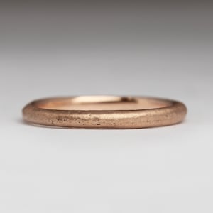 May include: A simple, brushed rose gold wedding band. The band is smooth and has a matte finish.