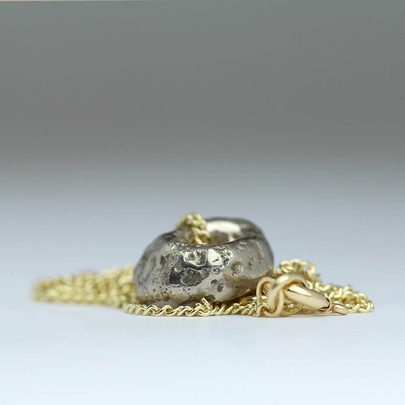 Puede incluir: Un collar de plata con un colgante redondo texturizado. El colgante est&aacute; unido a una cadena de oro.