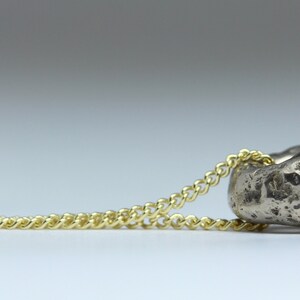 Puede incluir: Un collar con un colgante de plata en forma de coraz&oacute;n texturizado y rugoso. La cadena es de oro y tiene un dise&ntilde;o delicado y enlazado.