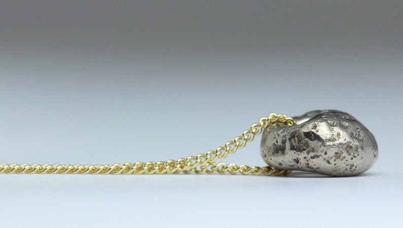 Puede incluir: Un collar con un colgante de plata en forma de coraz&oacute;n texturizado y rugoso. La cadena es de oro y tiene un dise&ntilde;o delicado y enlazado.