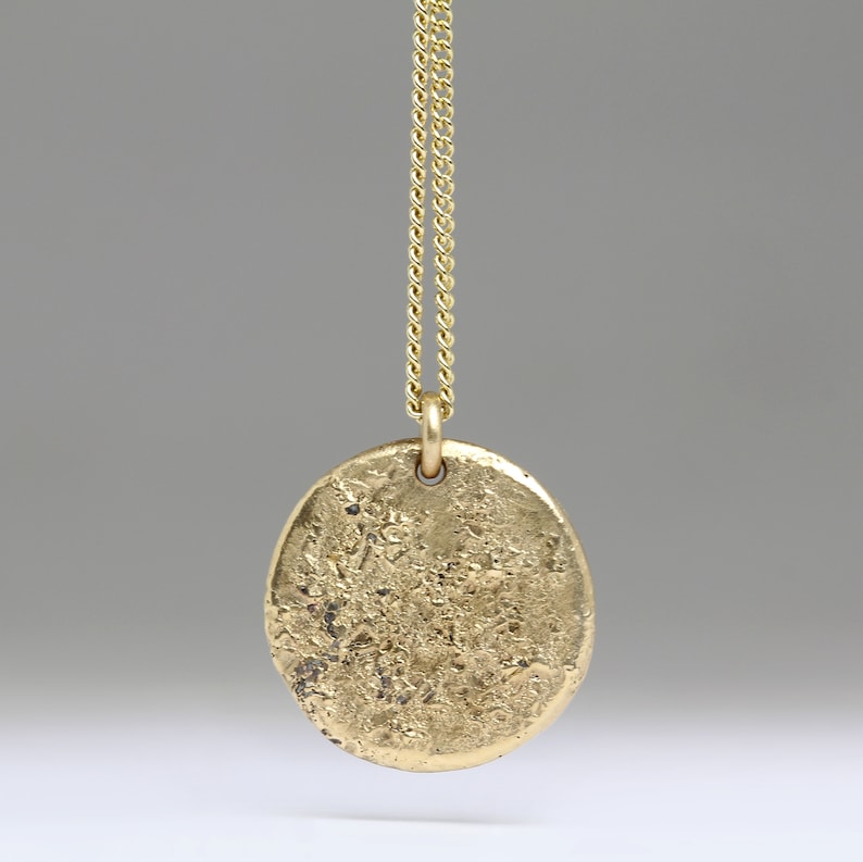 May include: A gold chain necklace with a large, oval-shaped pendant. The pendant has a textured, hammered finish.