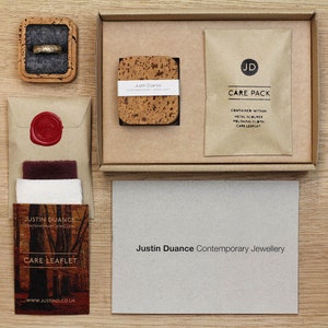 May include: A brown cardboard box with a care pack inside. The care pack contains a metal scrubber, a polishing cloth, and a care leaflet. The box also includes a small cork square with the text "Justin Duance Contemporary Jewellery".