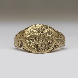 May include: A gold signet ring with a smooth, round top and a textured band.