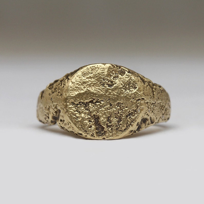 May include: A gold signet ring with a smooth, round top and a textured band.