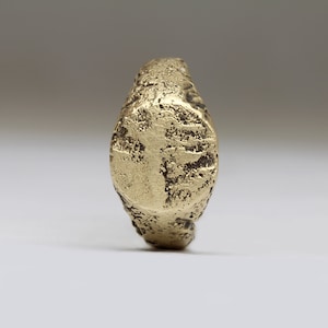 May include: A gold ring with a worn, textured surface. The ring has a raised, rectangular design on the top.