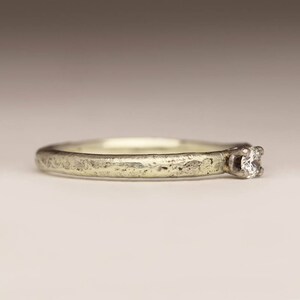 May include: A simple silver band ring with a single, small, round diamond set in the center.