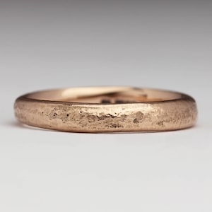 May include: A simple, rose gold wedding band with a textured finish.