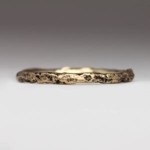 May include: A thin gold band ring with a textured, rough surface.