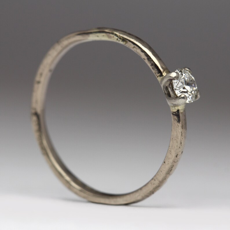 May include: A simple silver band ring with a single, clear diamond set in the center.