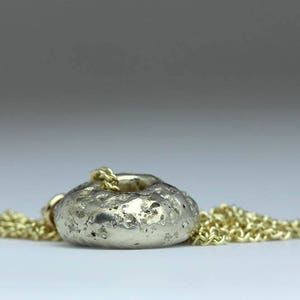Peut inclure: Un collier avec un pendentif rond en argent textur&eacute; en forme de beignet. Le pendentif a un trou au centre et est attach&eacute; &agrave; une cha&icirc;ne en or.