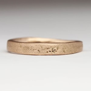 May include: A simple, brushed gold wedding band with a slightly rounded edge.