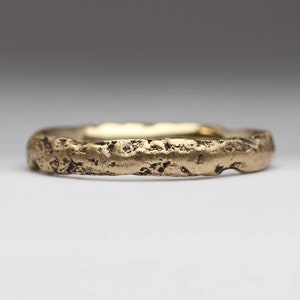 May include: A gold band ring with a textured, rough surface. The ring is a simple design with a wide band.