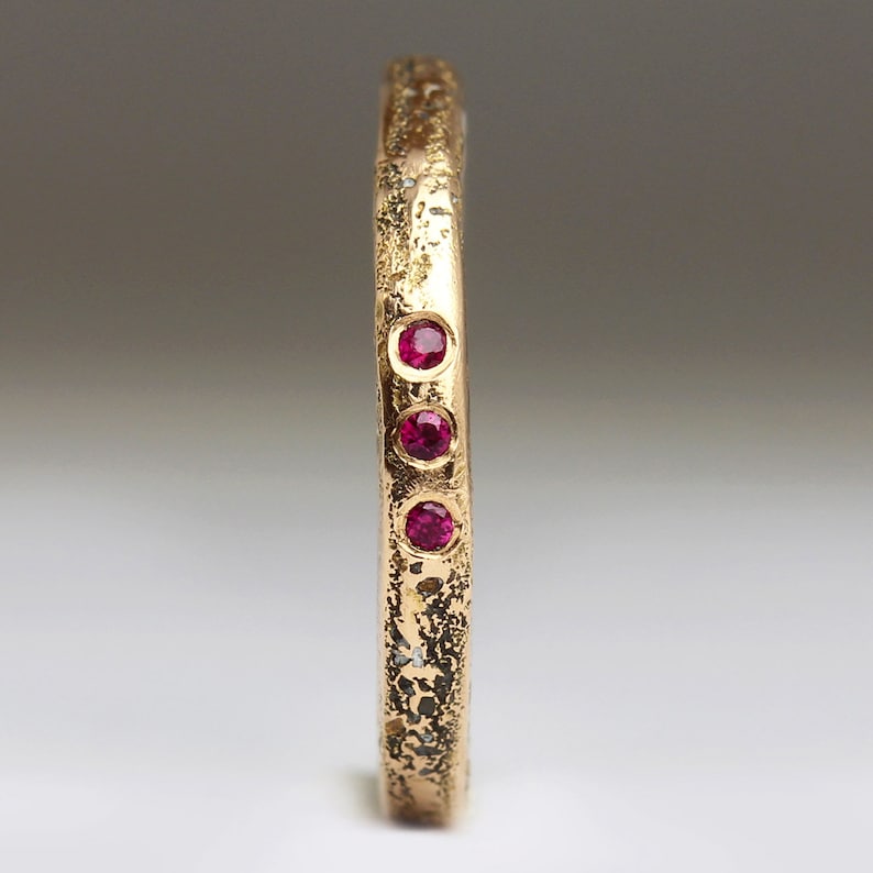 May include: A gold ring with a textured finish, showcasing three small, round, red gemstones. The ring's design is simple and elegant. The ring is suitable for everyday wear or special occasions.