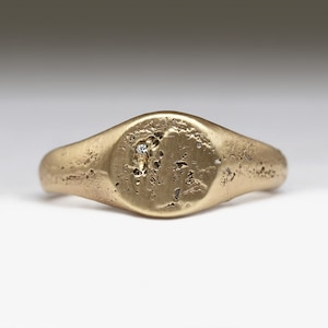 May include: A gold signet ring with a textured surface and a small diamond set in the center.