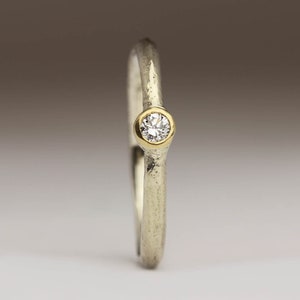 May include: A simple silver band ring with a textured finish and a single round diamond set in a gold bezel.