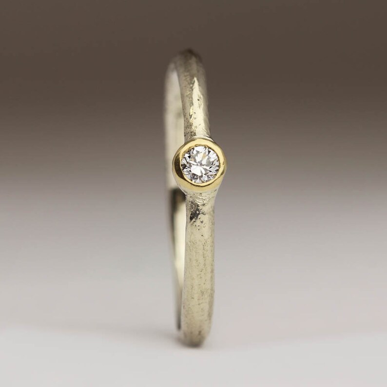 May include: A simple silver band ring with a textured finish and a single round diamond set in a gold bezel.