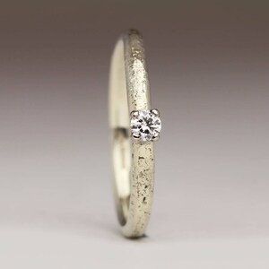 May include: A simple silver band ring with a single, small, round diamond set in the center.