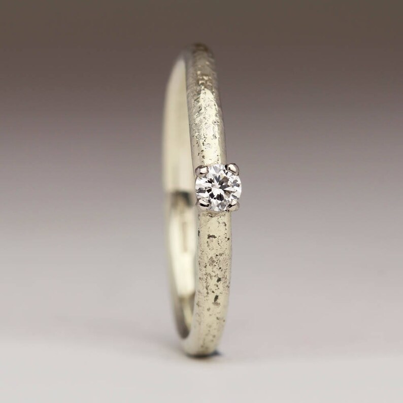 May include: A simple silver band ring with a single, small, round diamond set in the center.