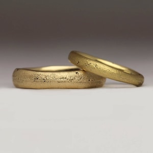 May include: Two gold wedding bands with a textured finish. The bands are stacked on top of each other.