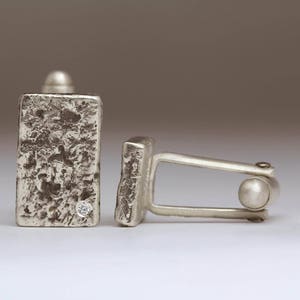 May include: A pair of silver cufflinks with a textured finish. One cufflink features a small diamond.