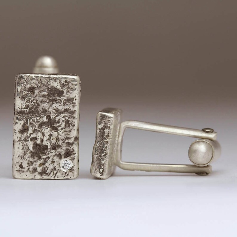 May include: A pair of silver cufflinks with a textured finish. One cufflink features a small diamond.