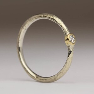 May include: A silver ring with a textured band and a single, small, round diamond set in a gold bezel.
