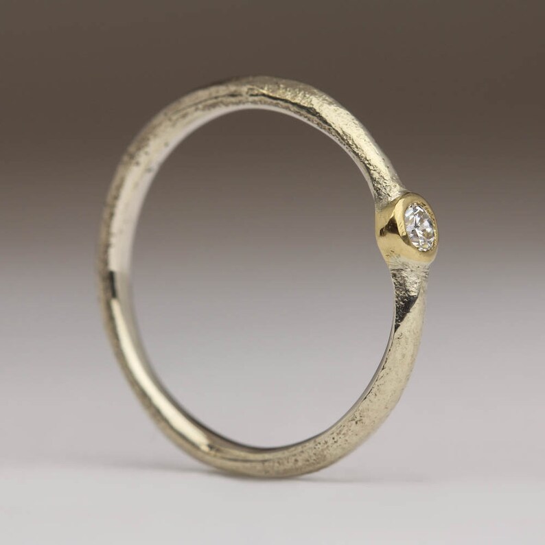May include: A silver ring with a textured band and a single, small, round diamond set in a gold bezel.