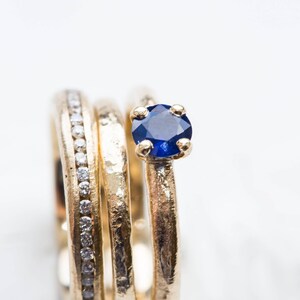 May include: Three gold rings stacked together, one with a small blue sapphire gemstone. The ring with the sapphire is on top of the stack.