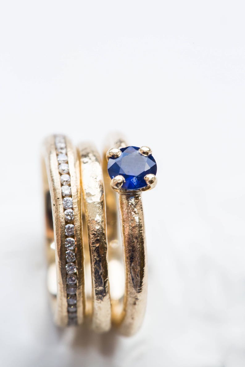 May include: Three gold rings stacked together, one with a small blue sapphire gemstone. The ring with the sapphire is on top of the stack.