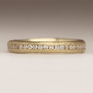 May include: A thin gold band with a row of small diamonds set in a channel setting.