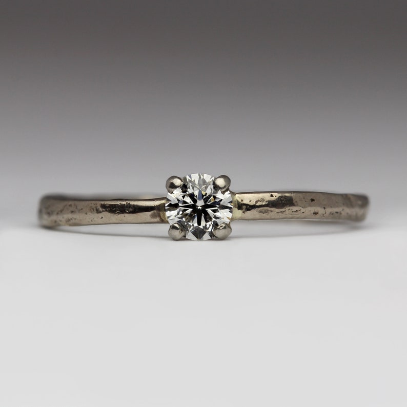 May include: A simple silver band ring with a single round diamond set in the center.
