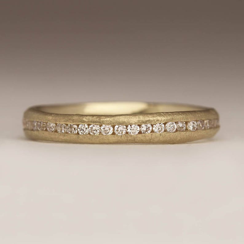 May include: A gold band with a row of small diamonds set into the metal. The band has a textured, hammered finish.