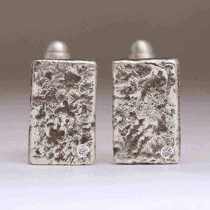 May include: A pair of silver earrings with a textured finish and a small diamond accent on each earring.