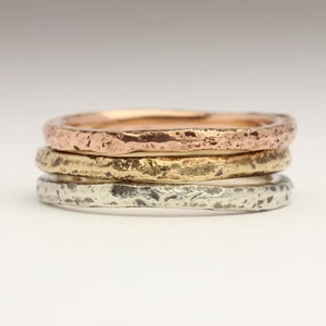 May include: Three thin, hammered metal bands in rose gold, yellow gold, and silver.