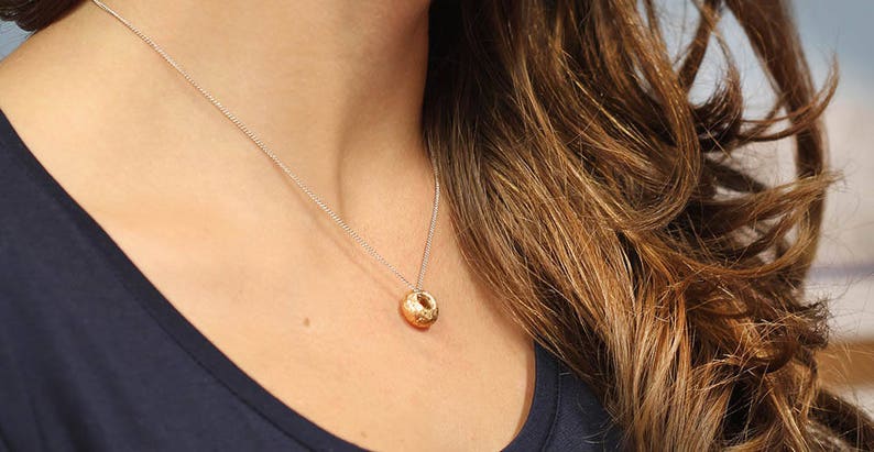 Peut inclure: Un collier en cha&icirc;ne argent avec un pendentif en or. Le pendentif est un orbe rond et textur&eacute;.