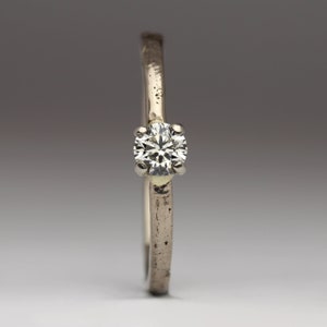 May include: A silver ring with a single, round, clear diamond.