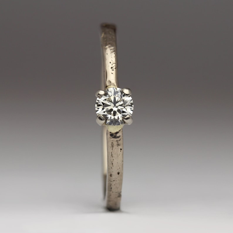 May include: A silver ring with a single, round, clear diamond.