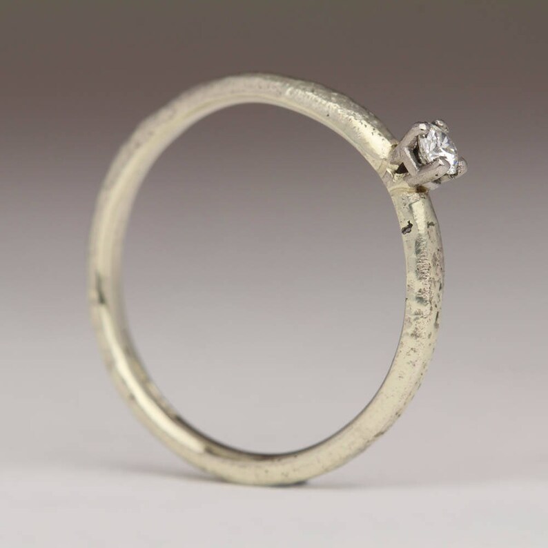 May include: A simple silver band ring with a single, small diamond set in the center.