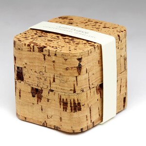 May include: A small, rectangular box made of cork with a white label that reads "Justin Duance Contemporary Jewellery".