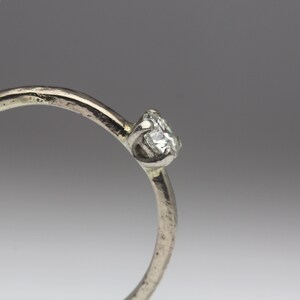 May include: A simple silver band ring with a single, small, round diamond set in the center.