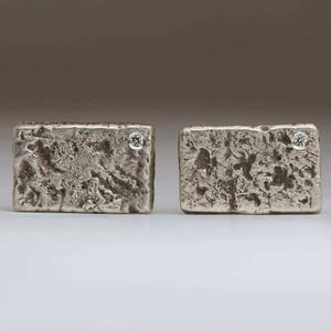 May include: A pair of silver cufflinks with a textured surface and a small diamond set in each cufflink.