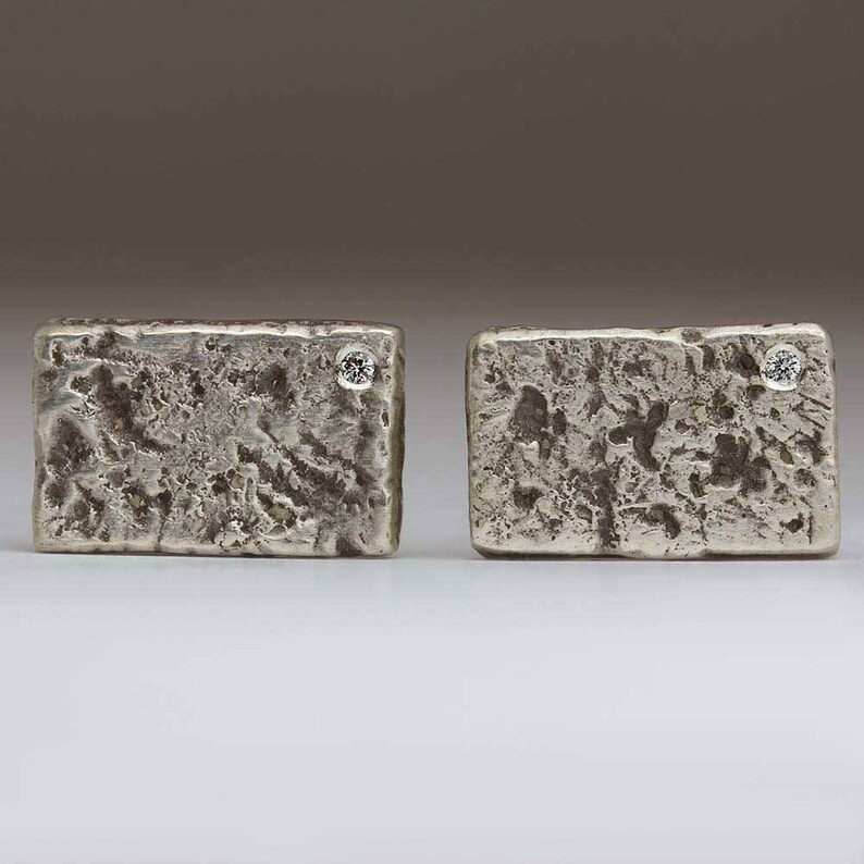 May include: A pair of silver cufflinks with a textured surface and a small diamond set in each cufflink.